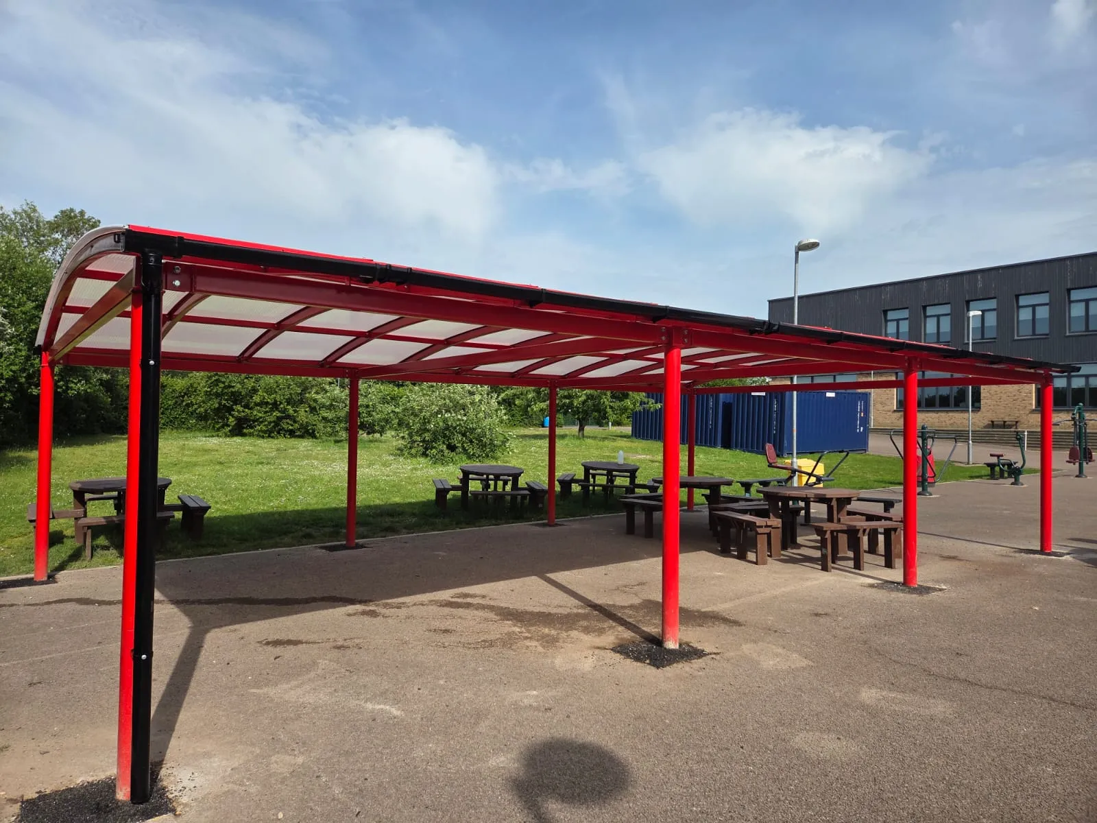 Large red steel canopy covering outdoor picnic benches and seating on school grounds