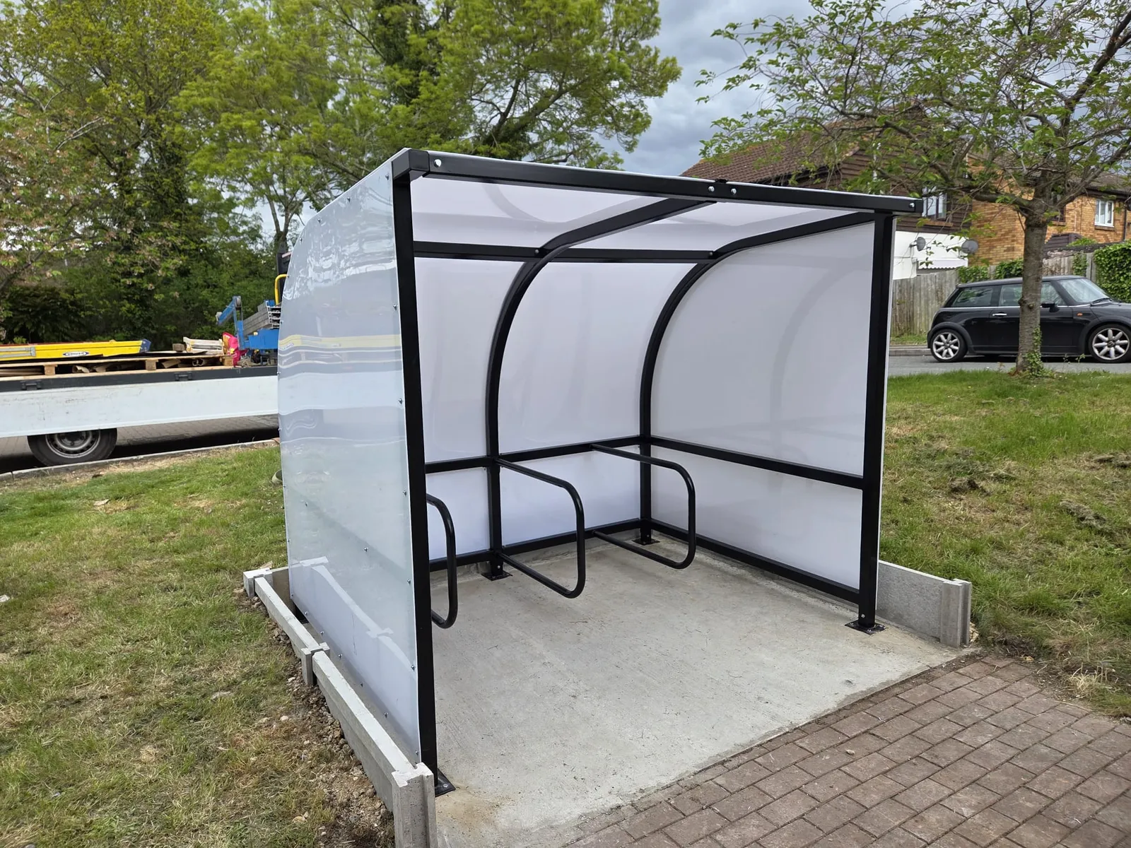 Hexagonal shelter with navy roof, glazed sides and timber bench seating beside a sports pitch